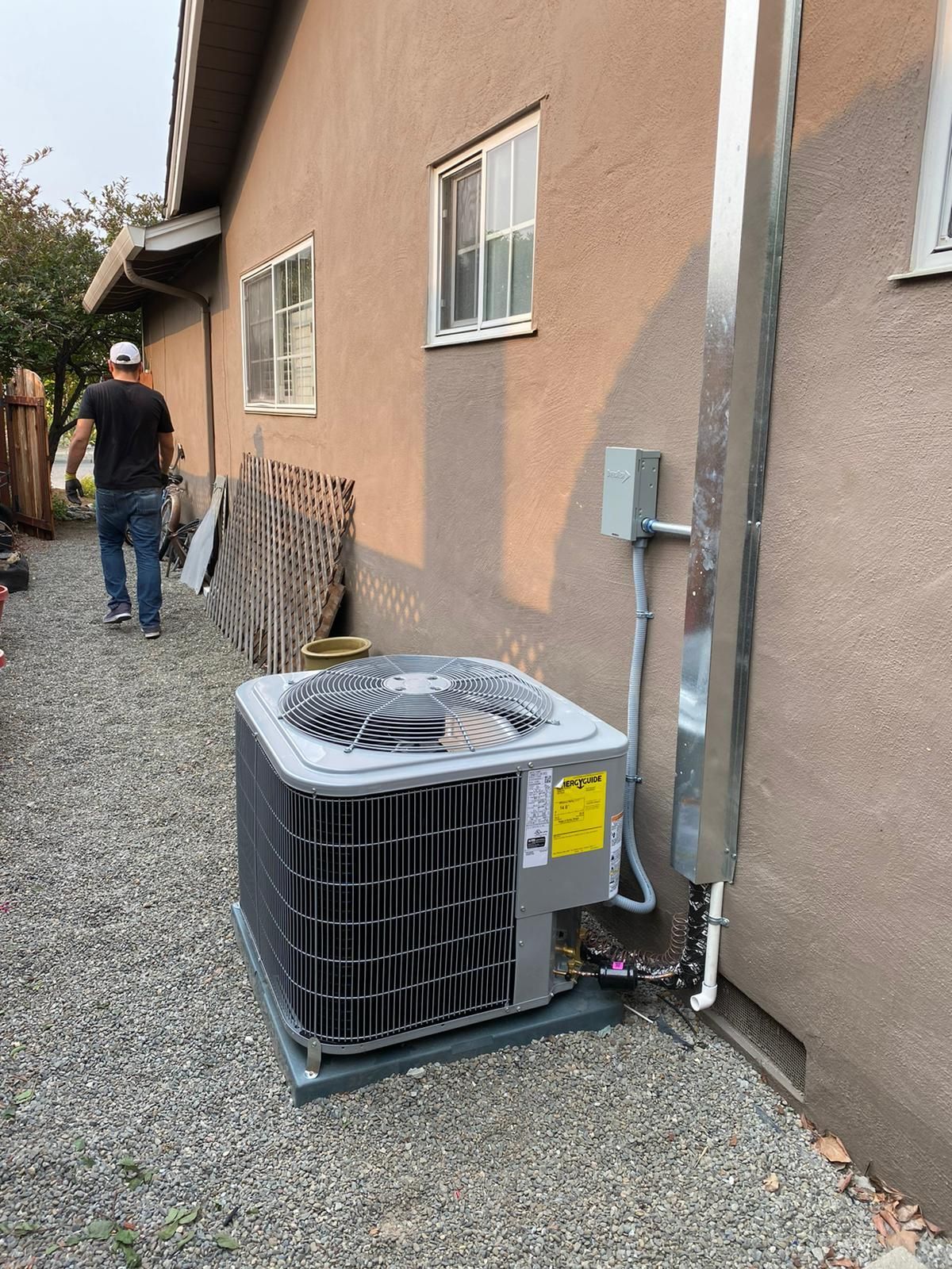 A man is walking down a gravel path next to a house with an air conditioner.