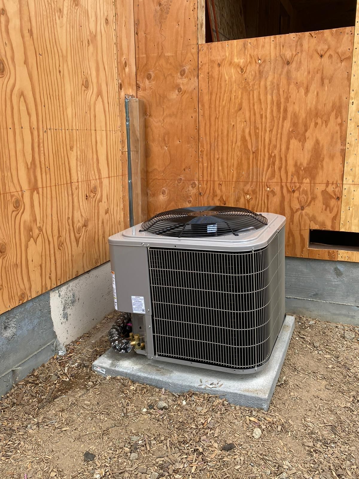 A large air conditioner is sitting on the ground in front of a wooden wall.