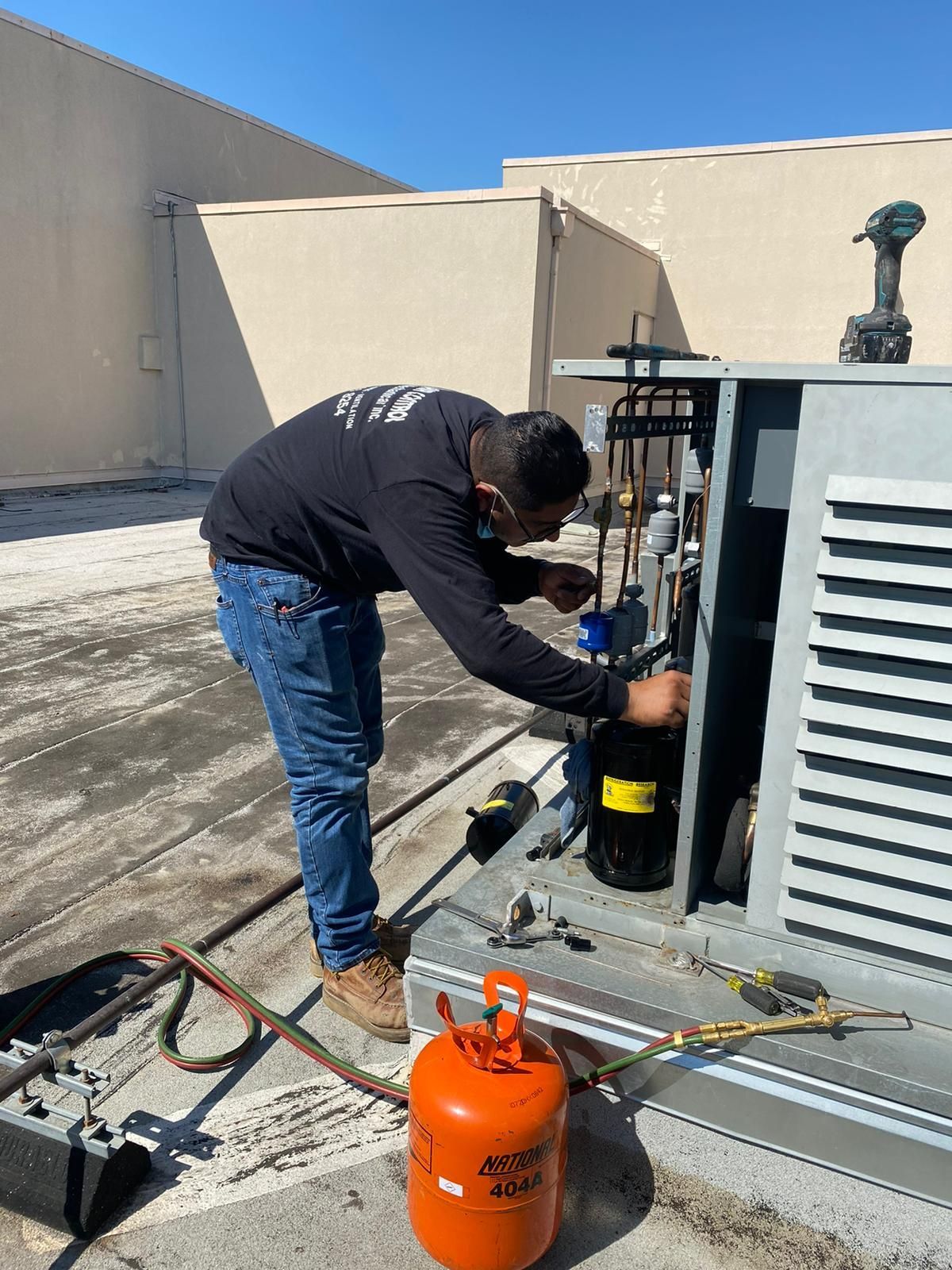 A man is working on an air conditioner on the roof of a building.