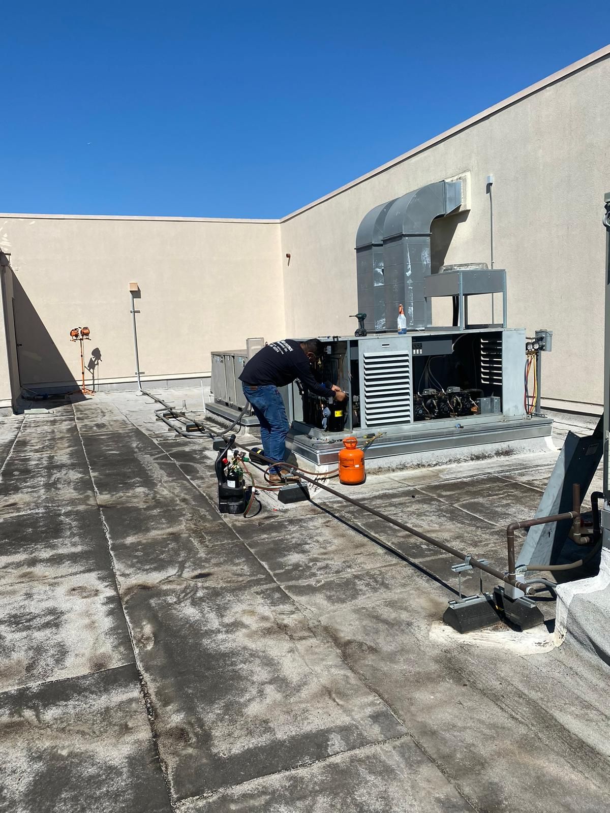 A man is working on an air conditioner on the roof of a building.