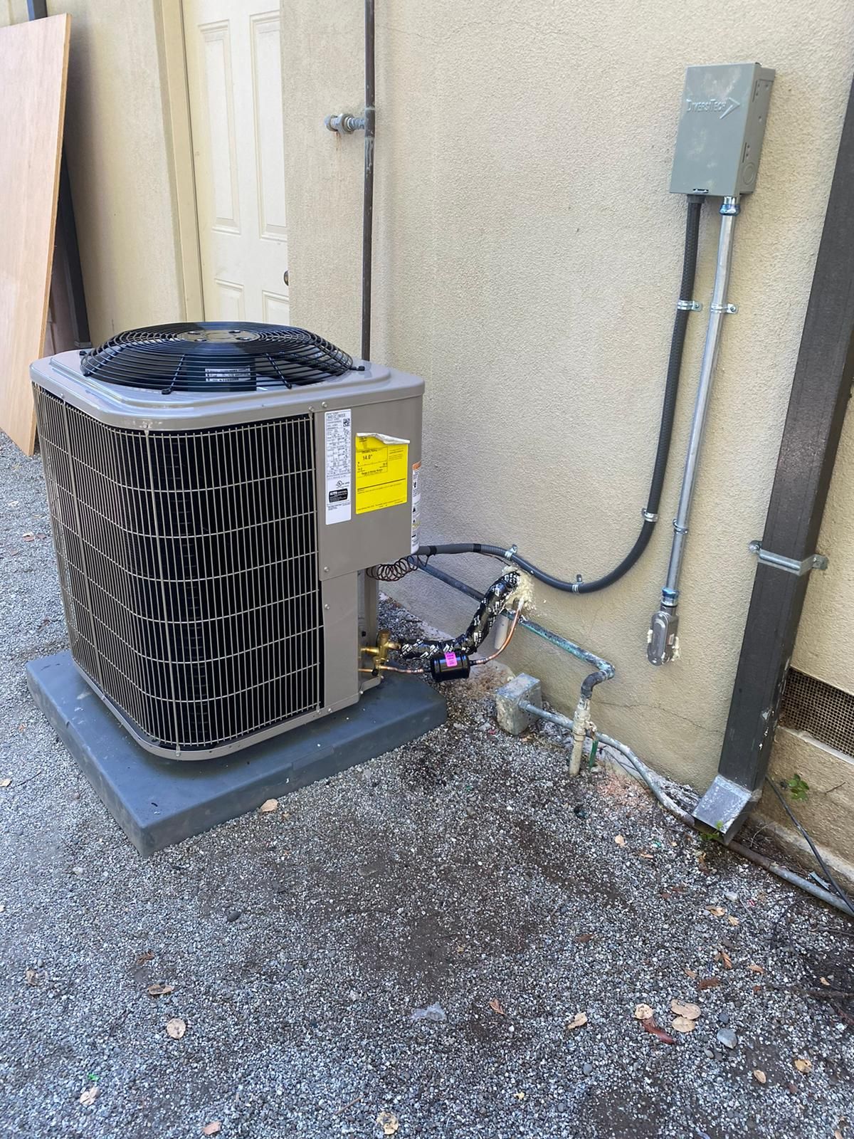 An air conditioner is sitting on top of a gravel driveway next to a building.