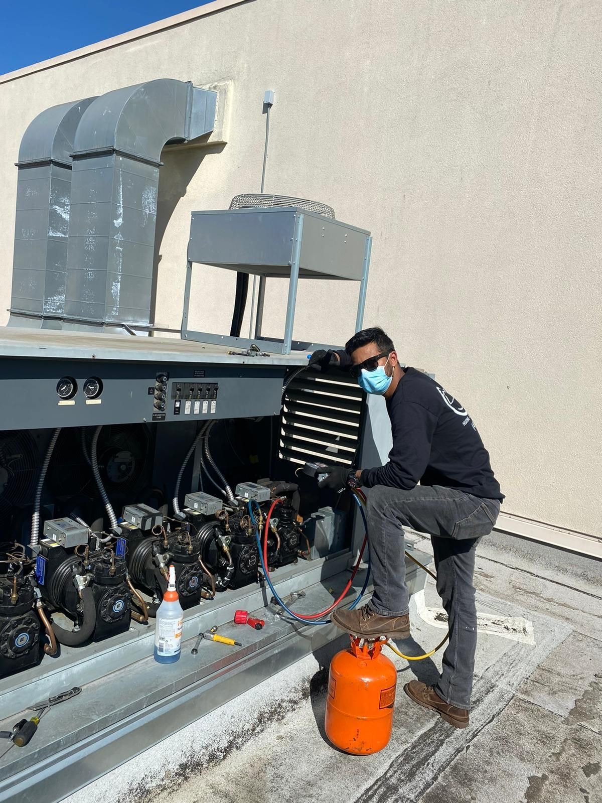 A man wearing a mask is working on an air conditioner on the roof of a building.
