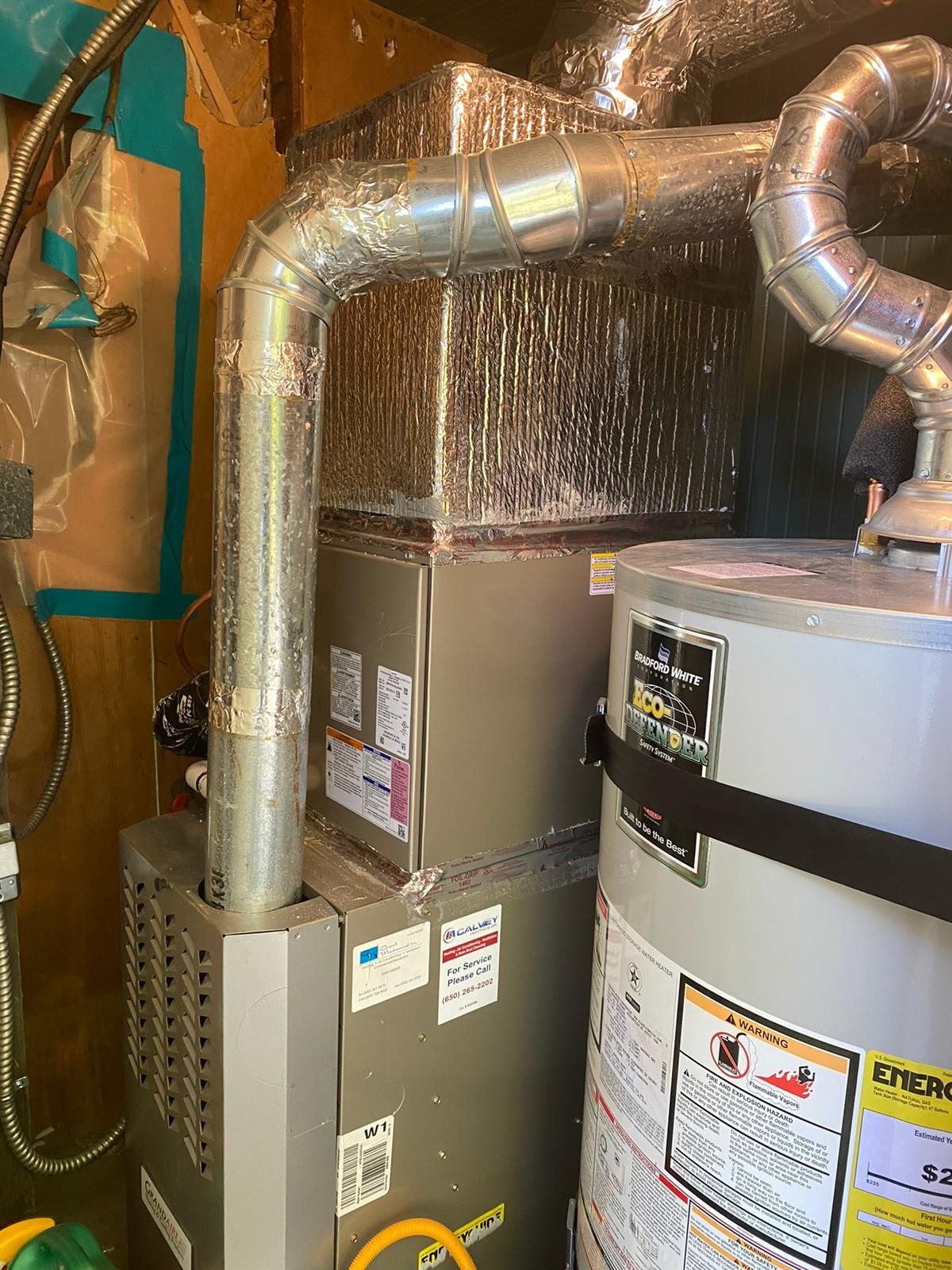 A water heater is sitting next to a furnace in a room.