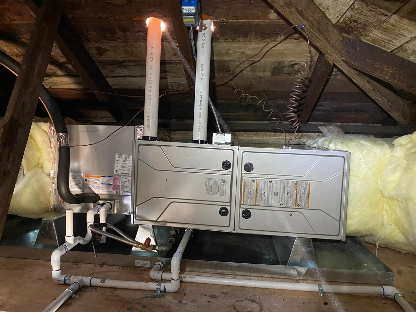 A stainless steel box is hanging from the ceiling of an attic.