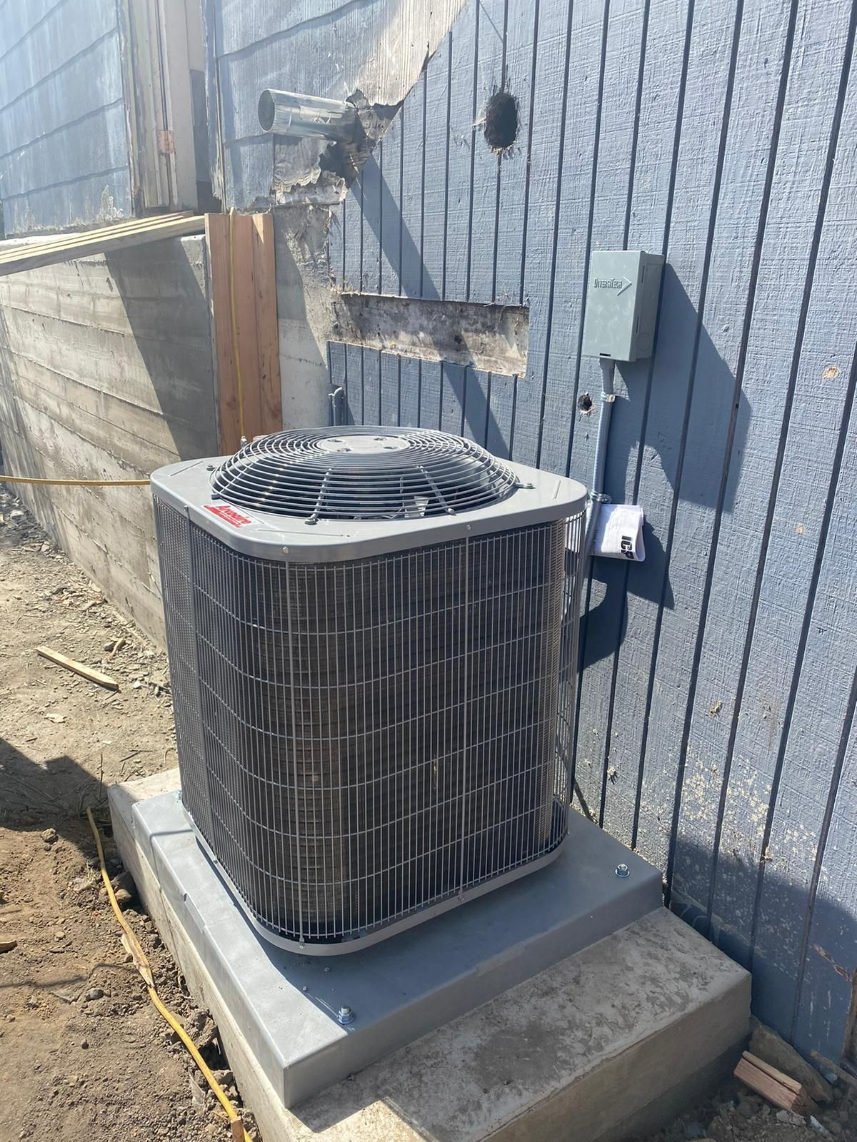 A large air conditioner is sitting on top of a concrete platform next to a building.