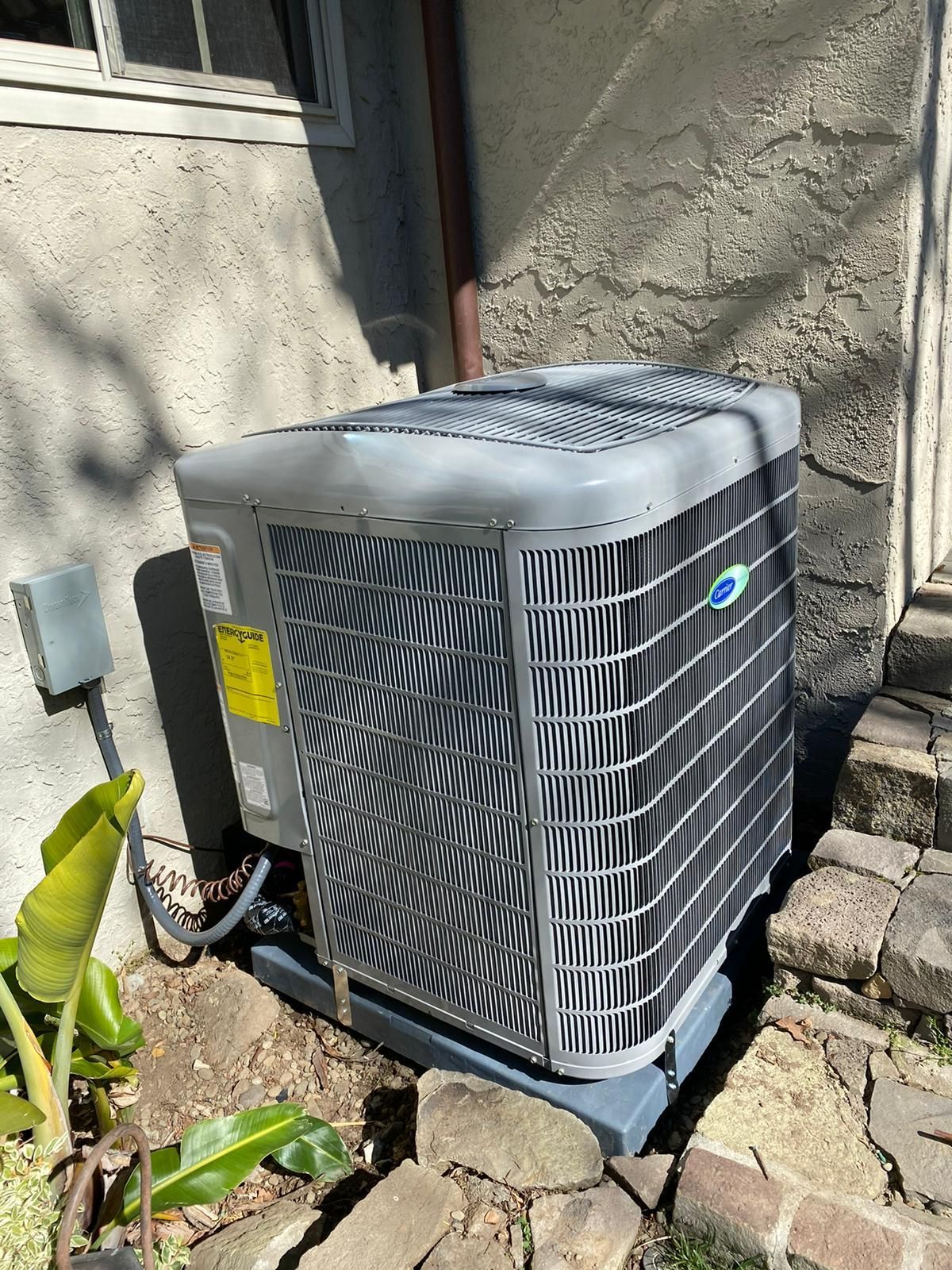 An air conditioner is sitting outside of a house next to a window.