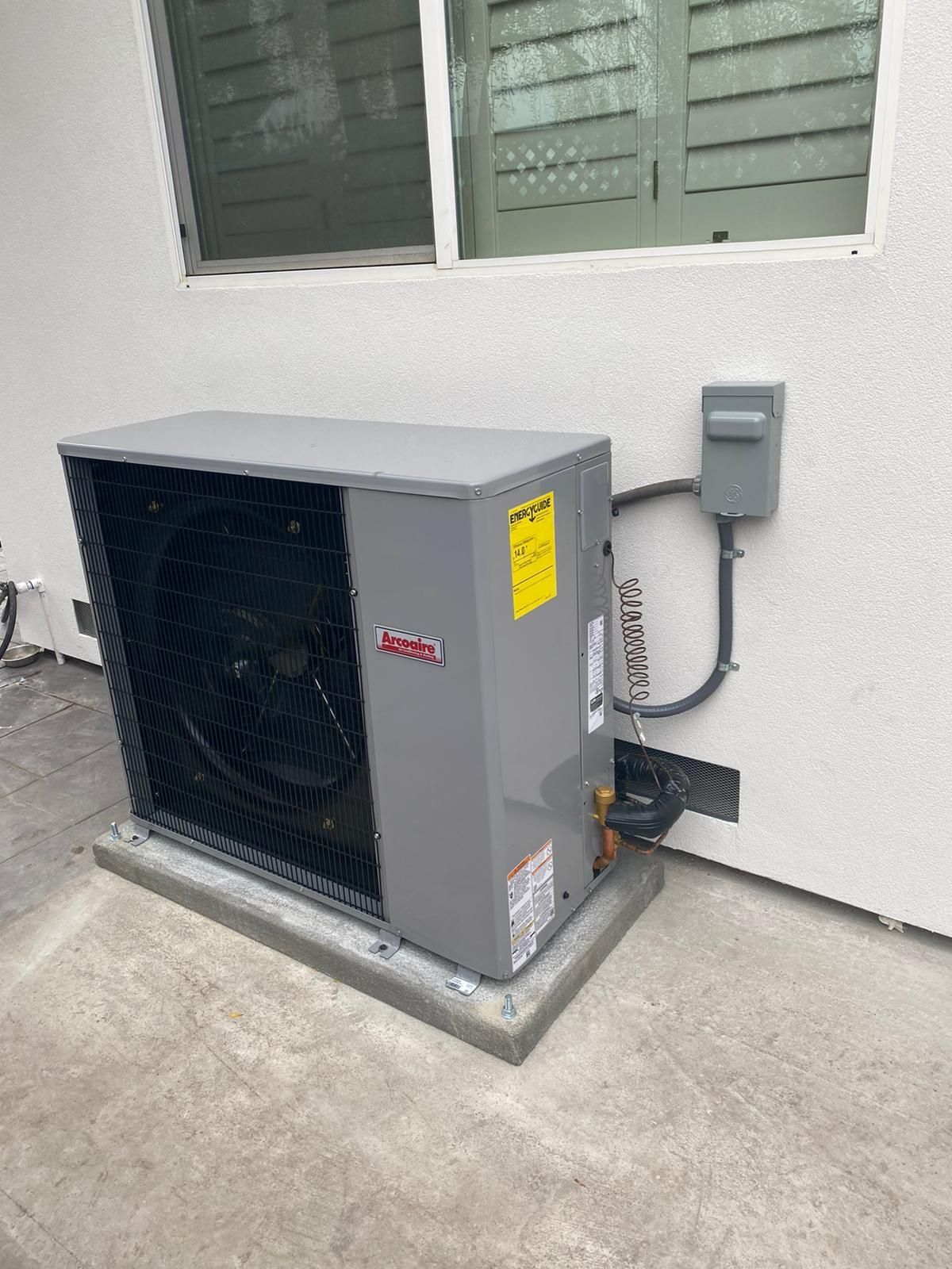 A large air conditioner is sitting on the side of a building next to a window.