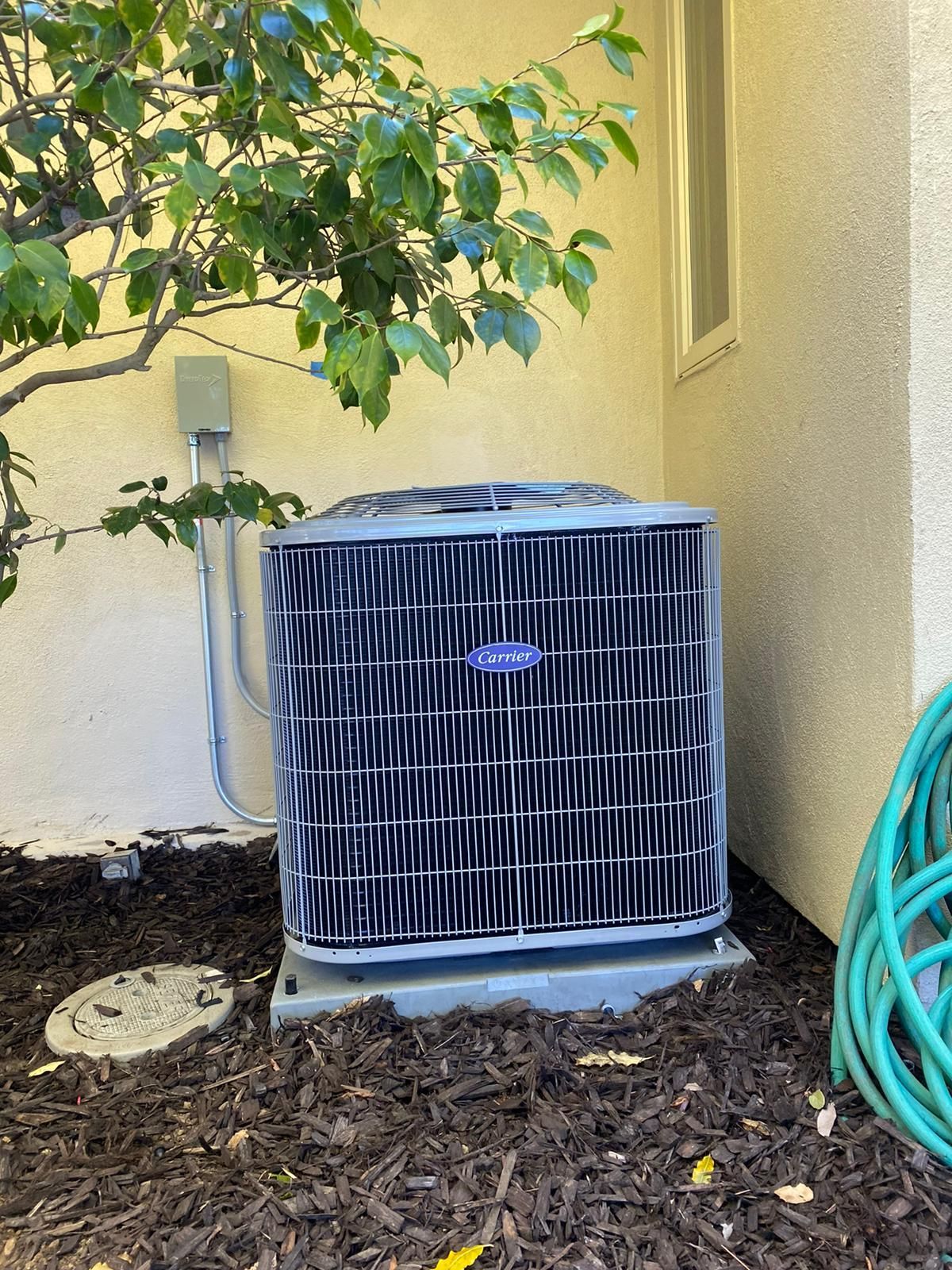 An air conditioner is sitting outside of a house next to a hose.