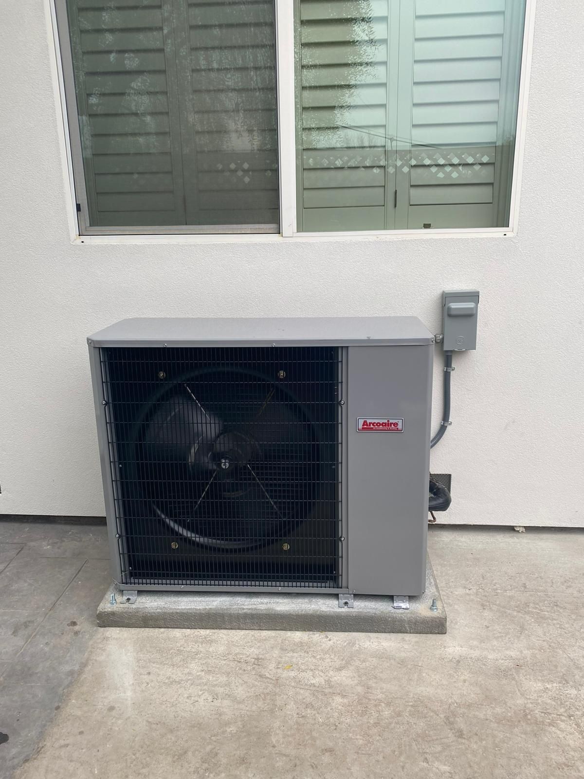 An air conditioner is sitting on the side of a building next to a window.