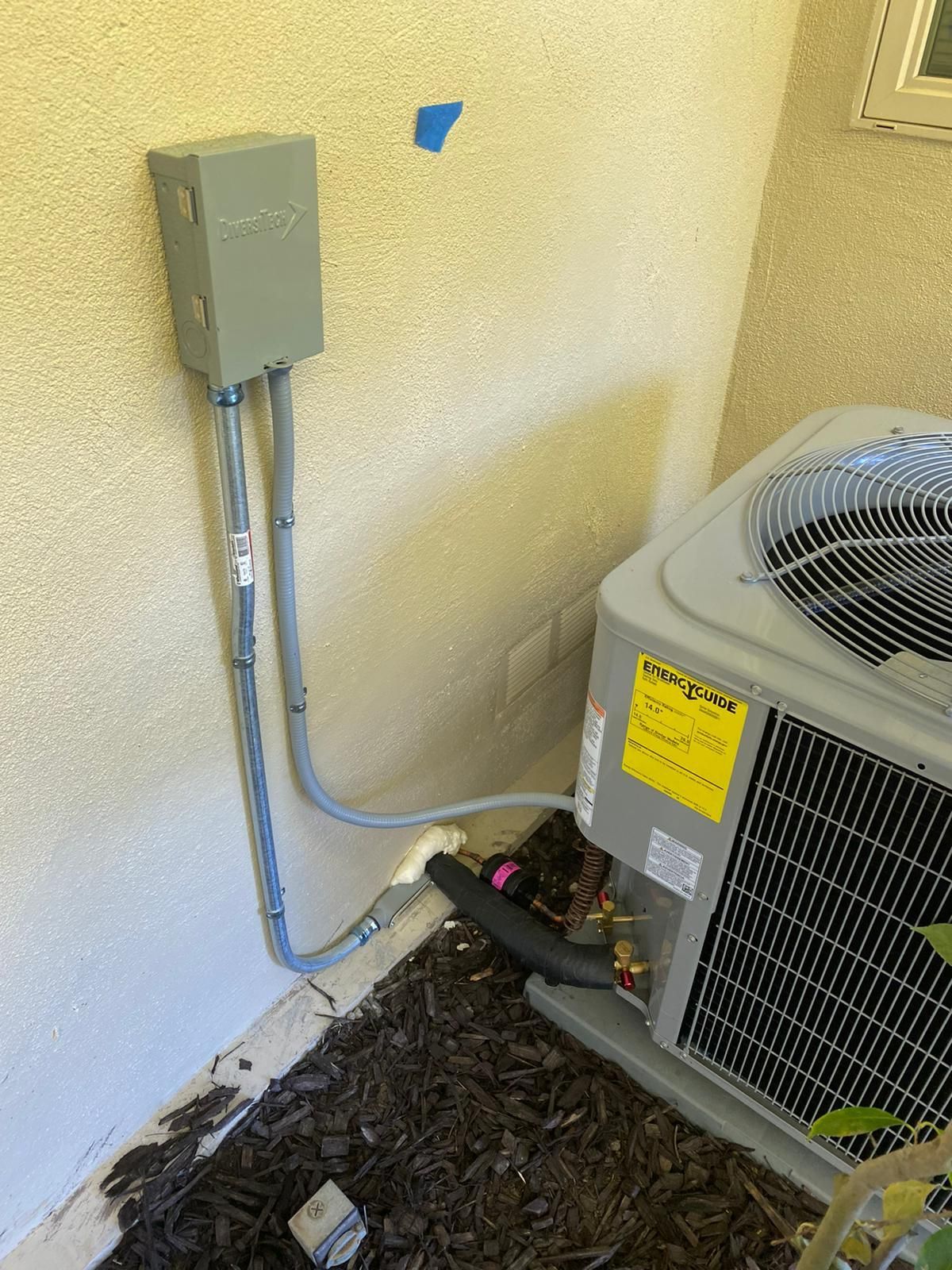 An air conditioner is sitting on the ground next to a wall.