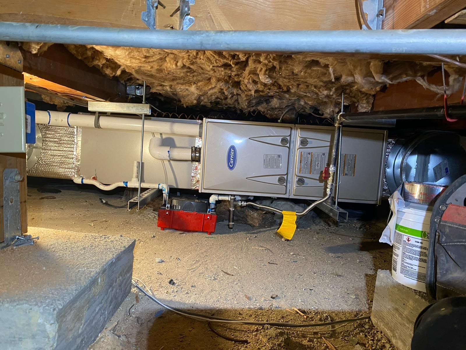 A furnace is sitting under a ceiling in a basement.