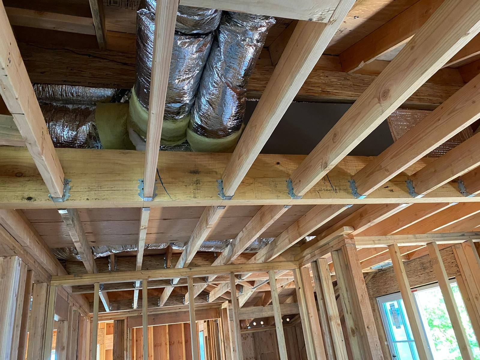 A house is being built with wooden beams and ducts coming out of the ceiling.