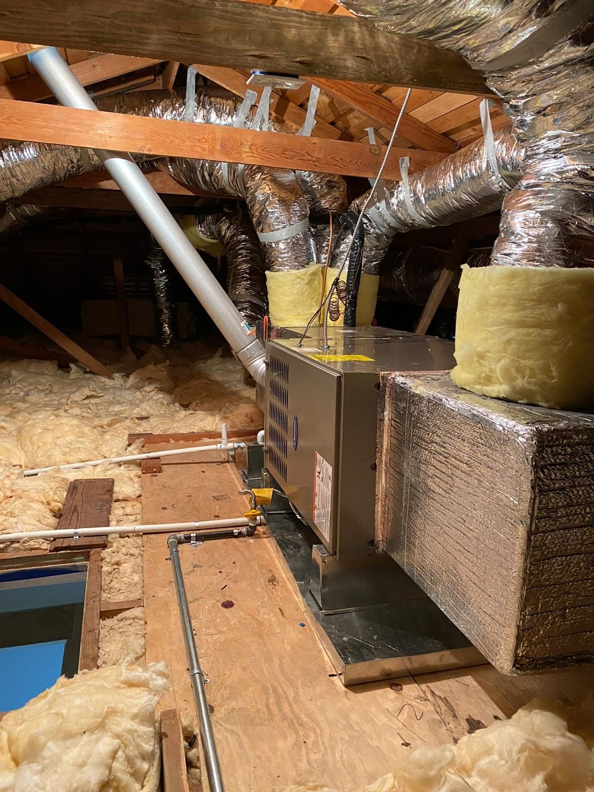 A picture of an attic with a heater and ducts.