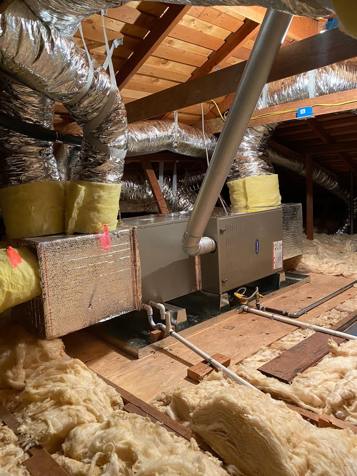 An attic with a lot of ducts and pipes hanging from the ceiling.