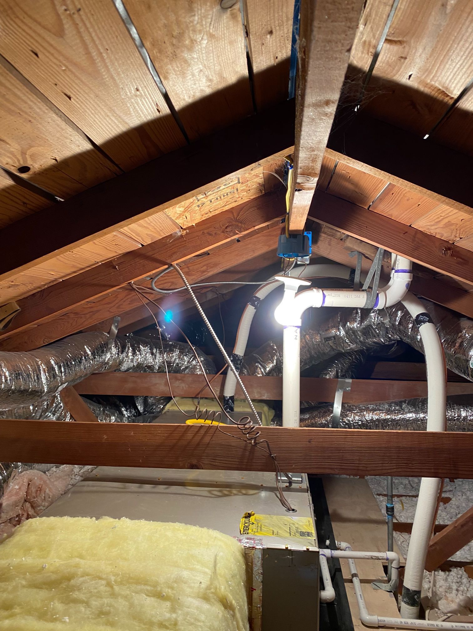 An attic with a lot of pipes hanging from the ceiling.
