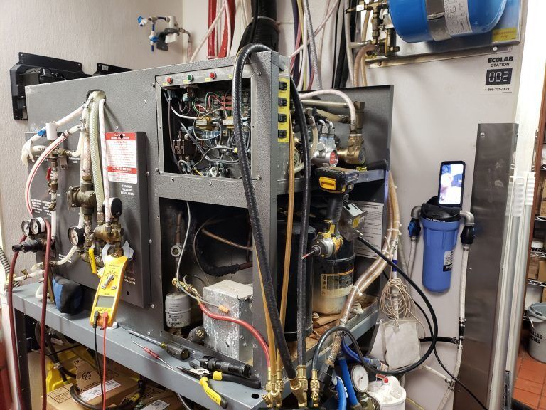 A machine is being worked on in a kitchen with a cell phone hanging on the wall.