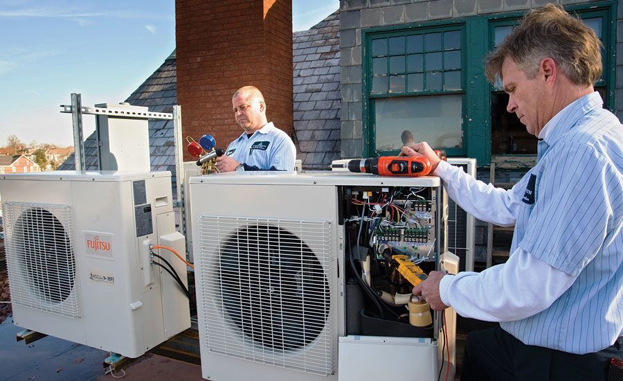Two men are working on an air conditioner on the roof of a building.