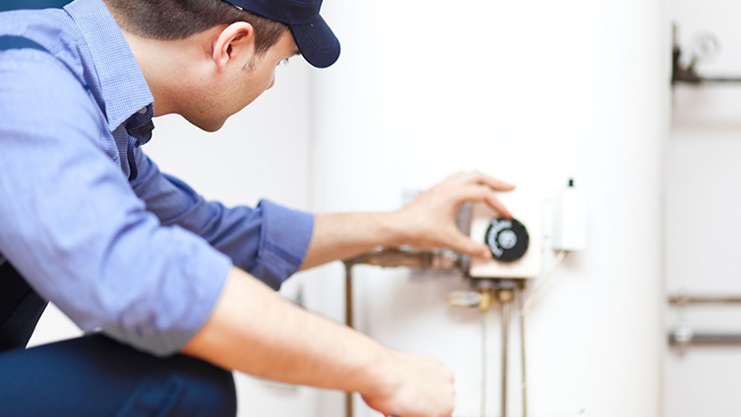 A man is kneeling down and working on a water heater.