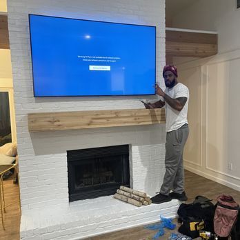 A man is standing in front of a fireplace with a flat screen tv mounted on the wall.