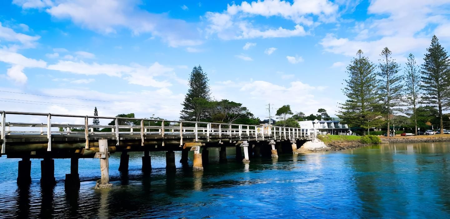 Wooden Bridge Over Blue Water Under a Cloudy Blue Sky — Blue Sky Roofing NSW In Brunswick Heads, NSW