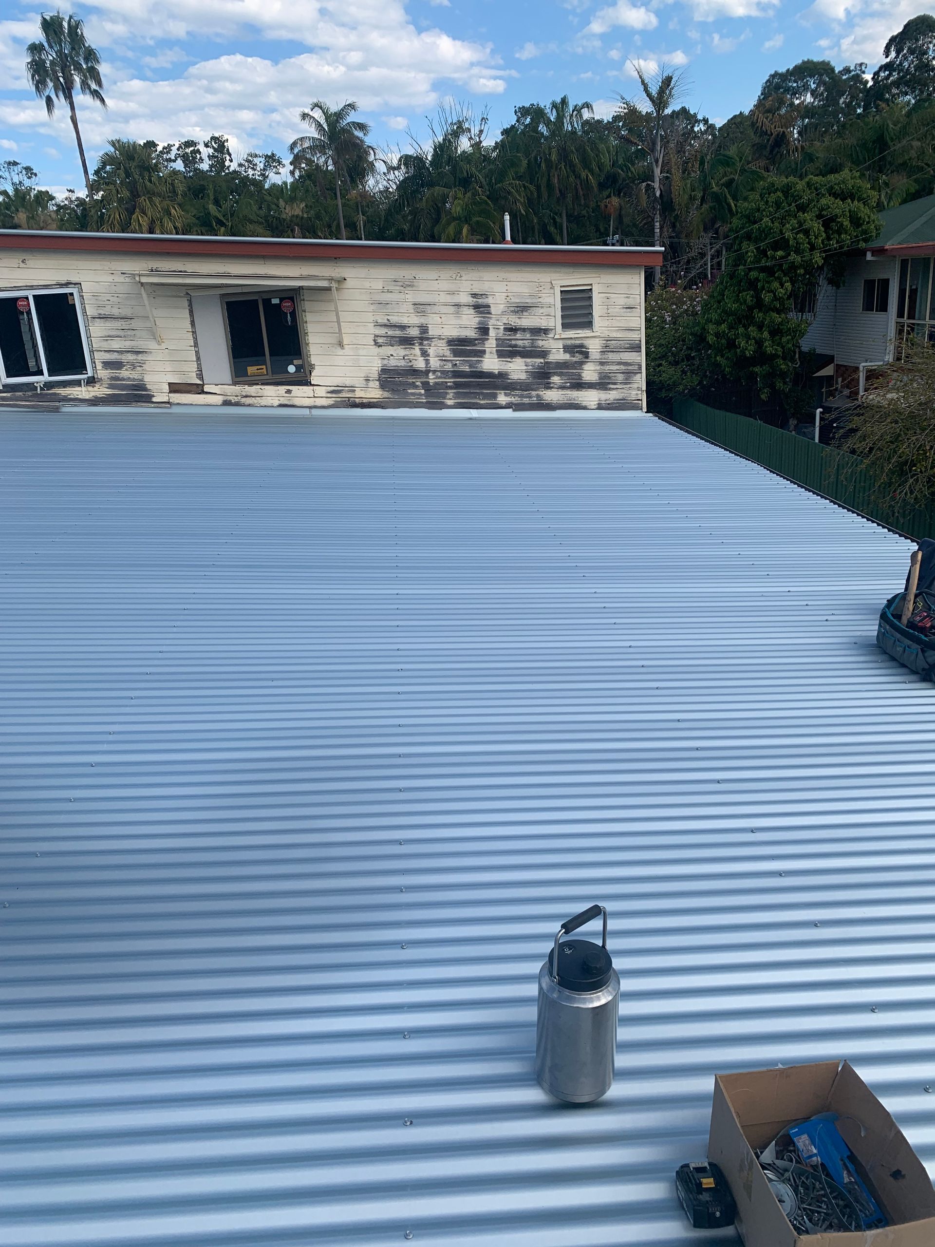 Metal corrugated roof with water bottle and tool box on it; building in the background.