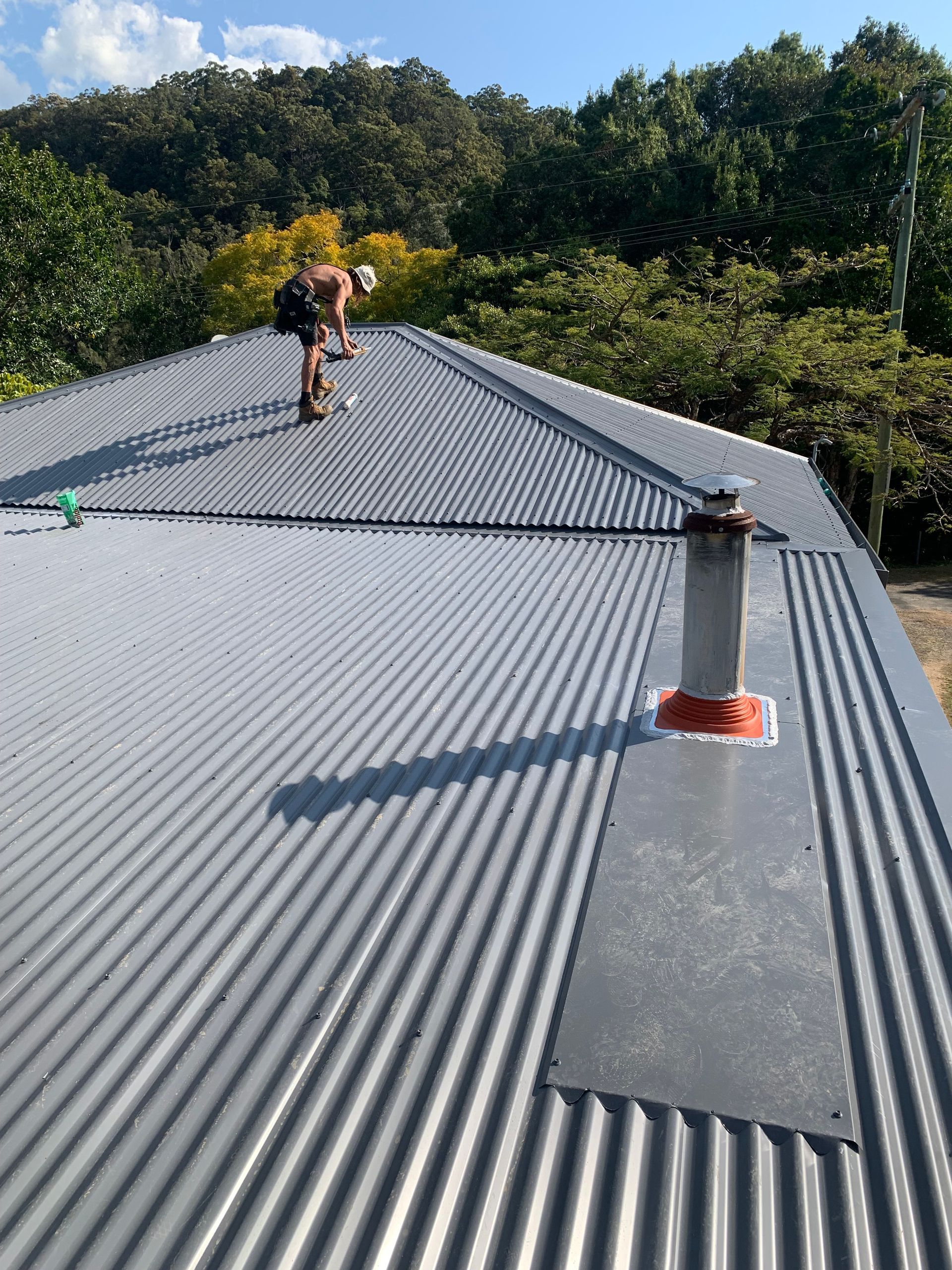 A navy blue roof with a worker on top doing repairs  — Blue Sky Roofing NSW In Ocean Shores, NSW