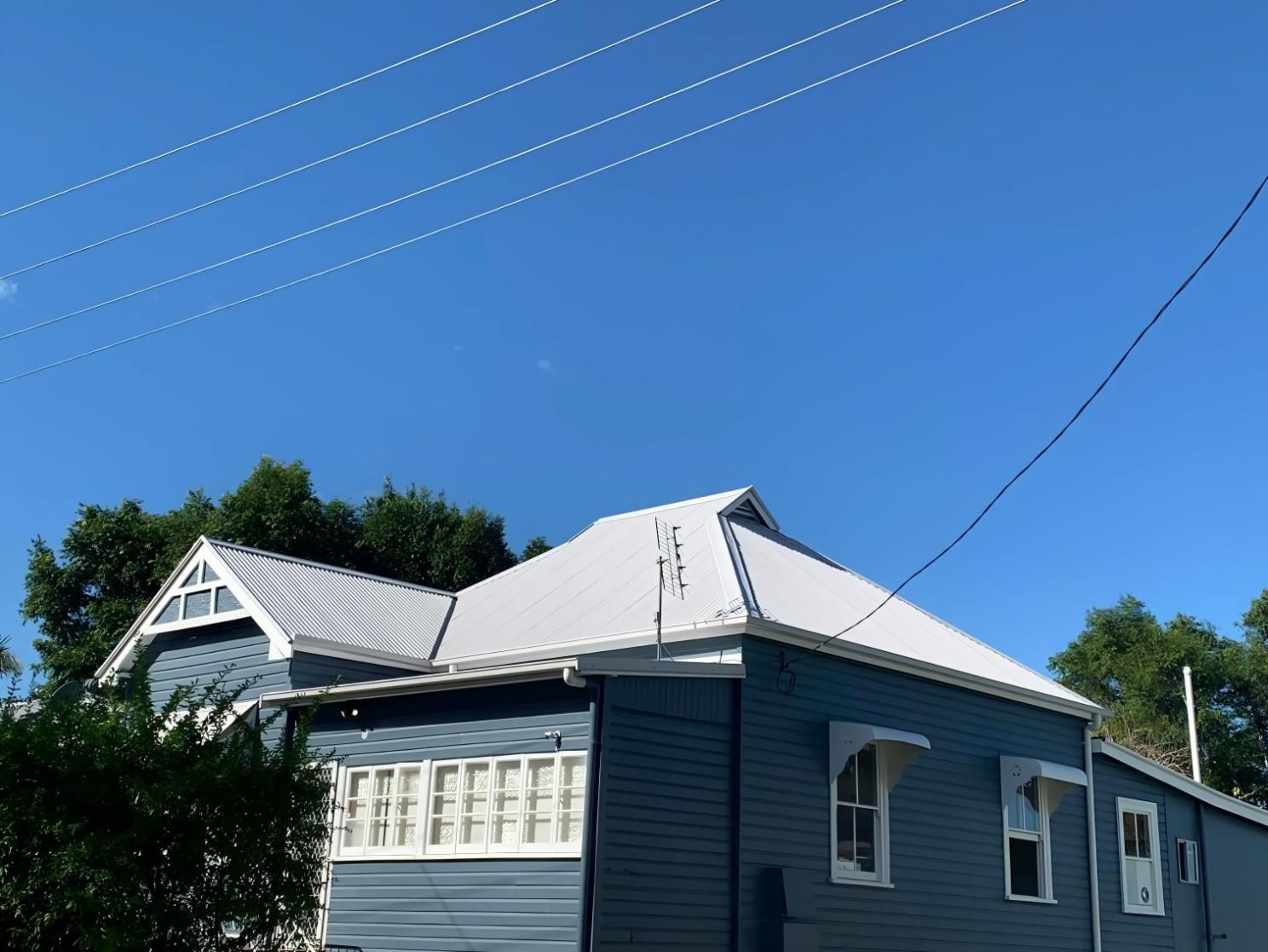 Blue House With White Trim and Roof Against a Clear Blue Sky. Power Lines Overhead — Blue Sky Roofing NSW In Mullumbimby, NSW