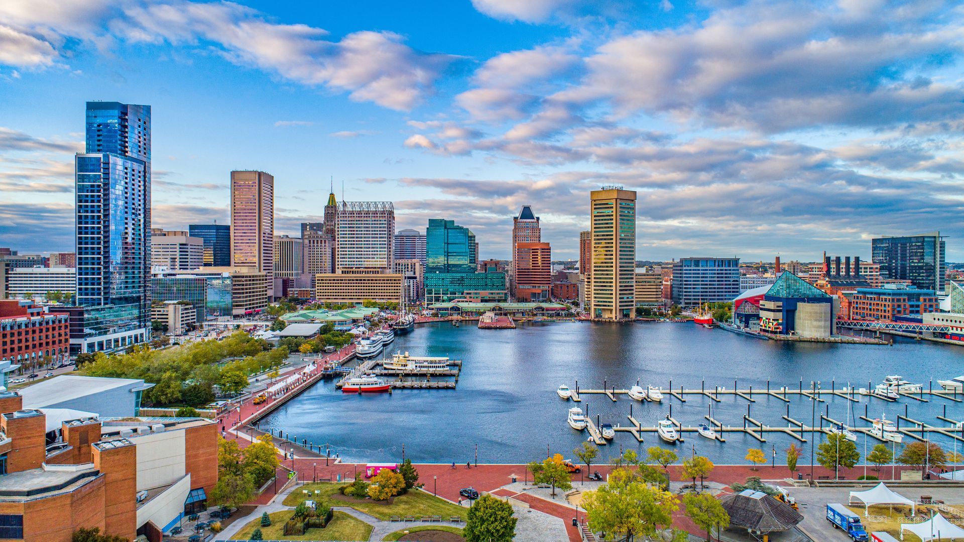 Baltimore Inner Harbor skyline with buildings, water, boats, and a bright sky.