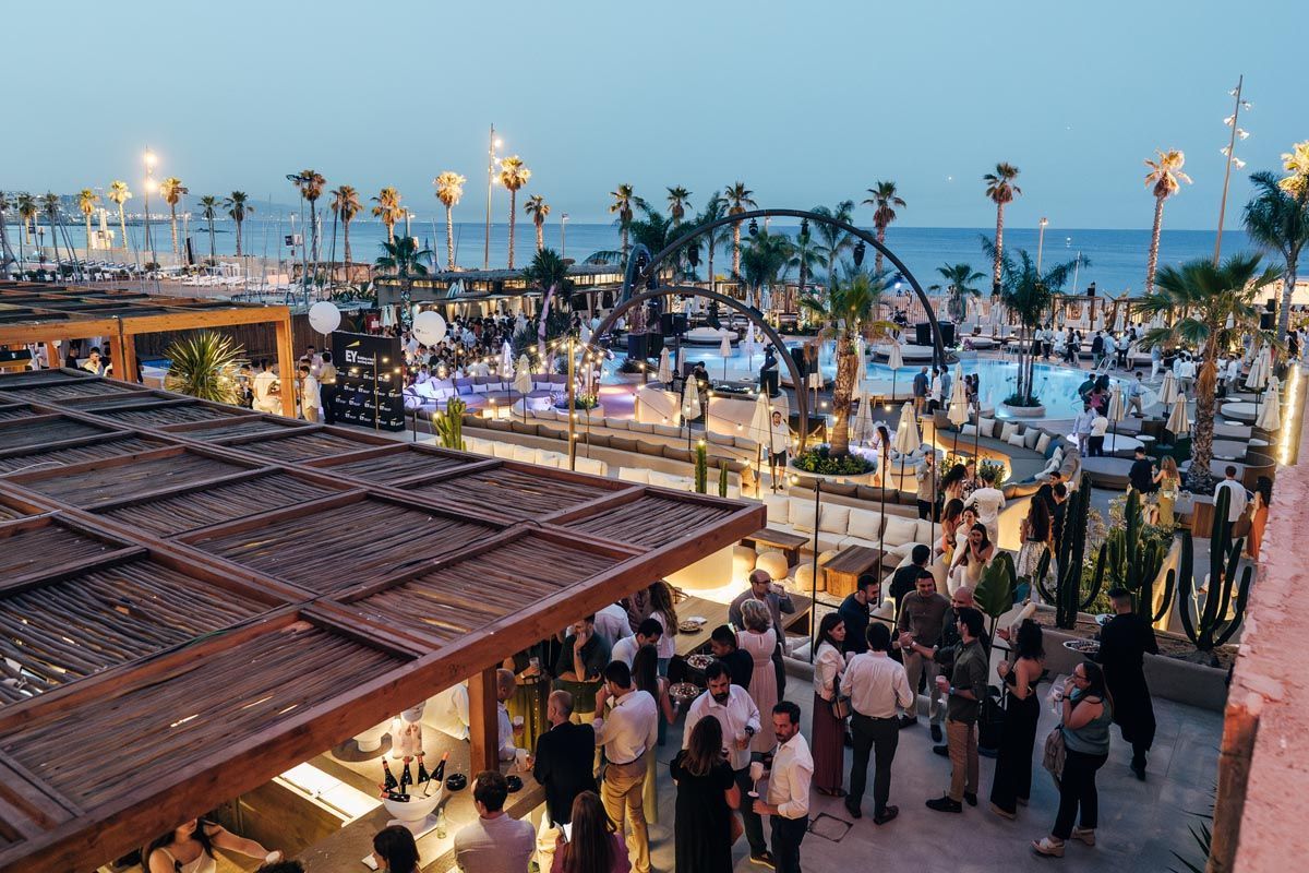 A swimming pool surrounded by palm trees and umbrellas next to a beach.