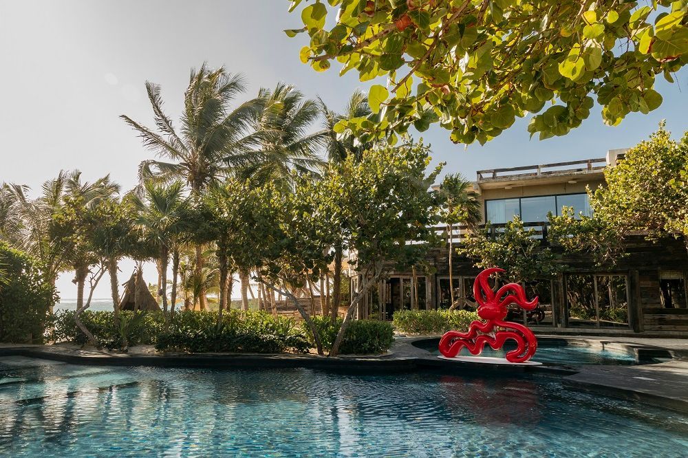 A large swimming pool surrounded by palm trees and a red octopus statue.