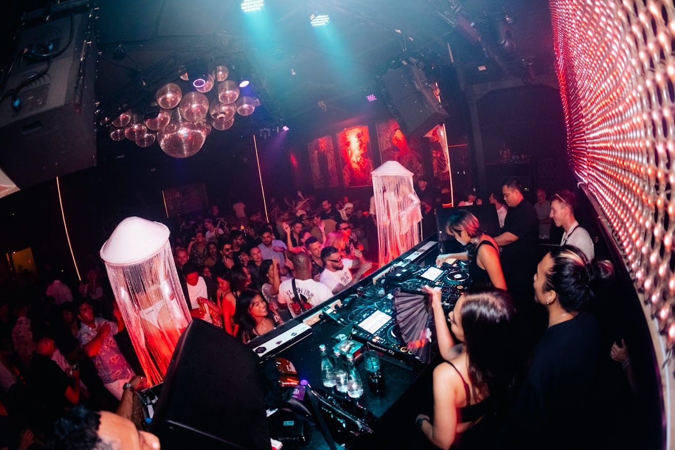 A group of people are standing around a dj booth in a club.