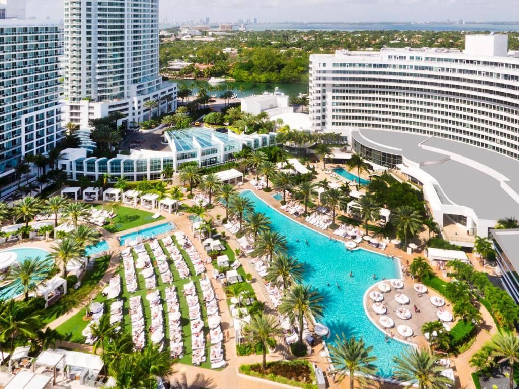 An aerial view of a large hotel with a large pool surrounded by palm trees.