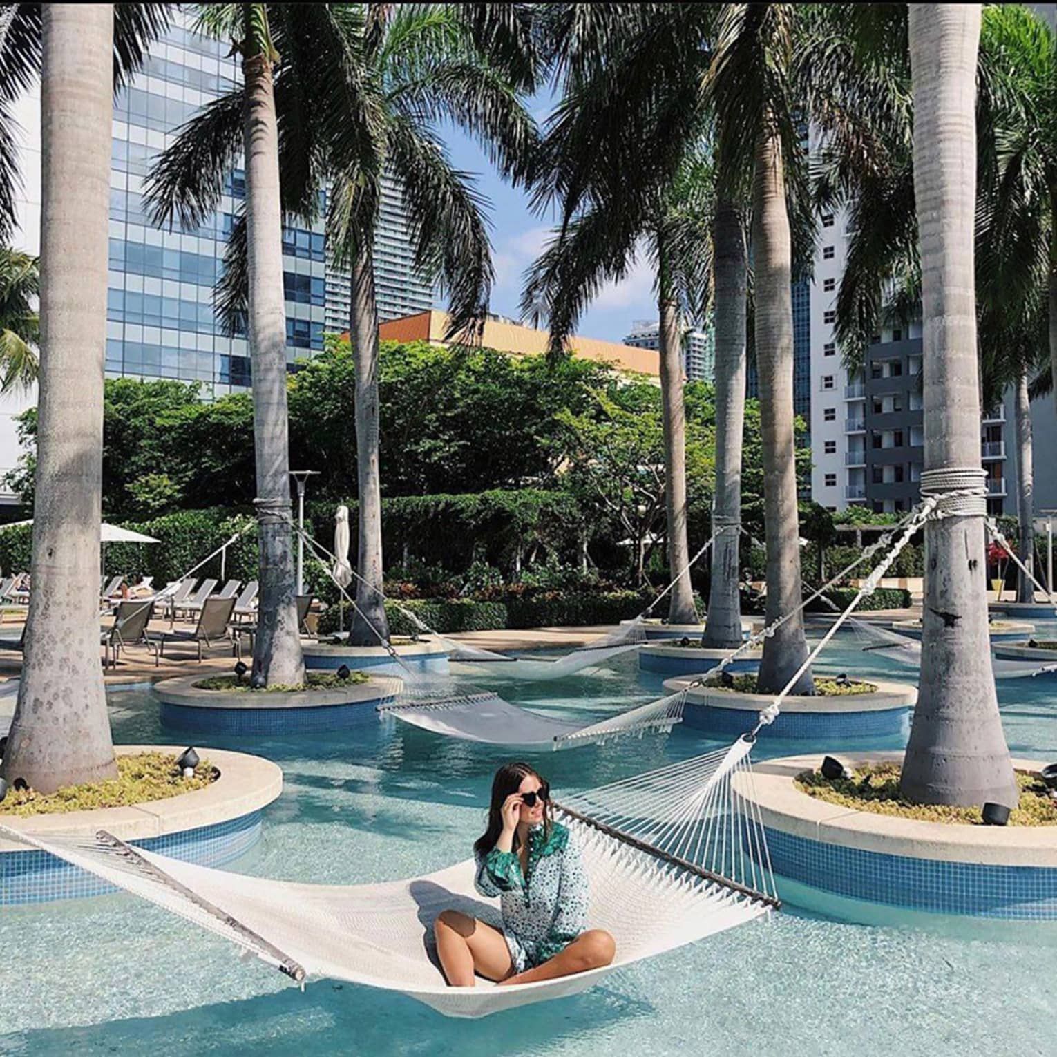 A woman is sitting in a hammock in a pool surrounded by palm trees