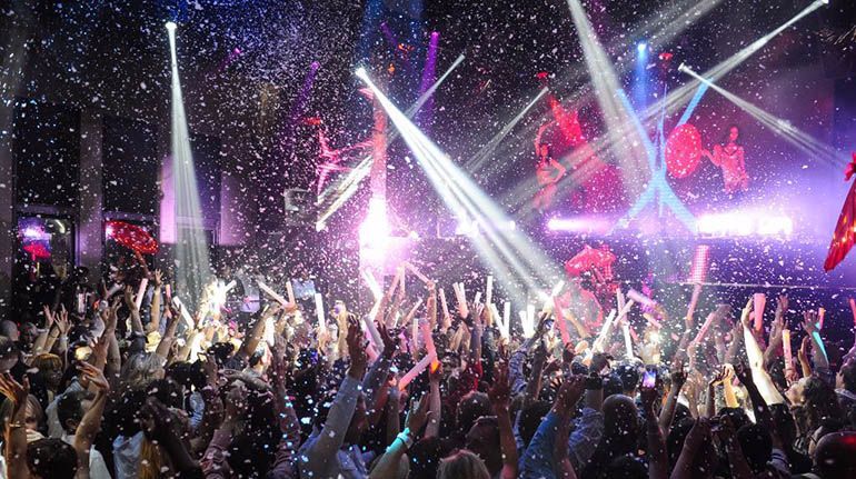 A crowd of people are dancing in a club with confetti falling from the ceiling.