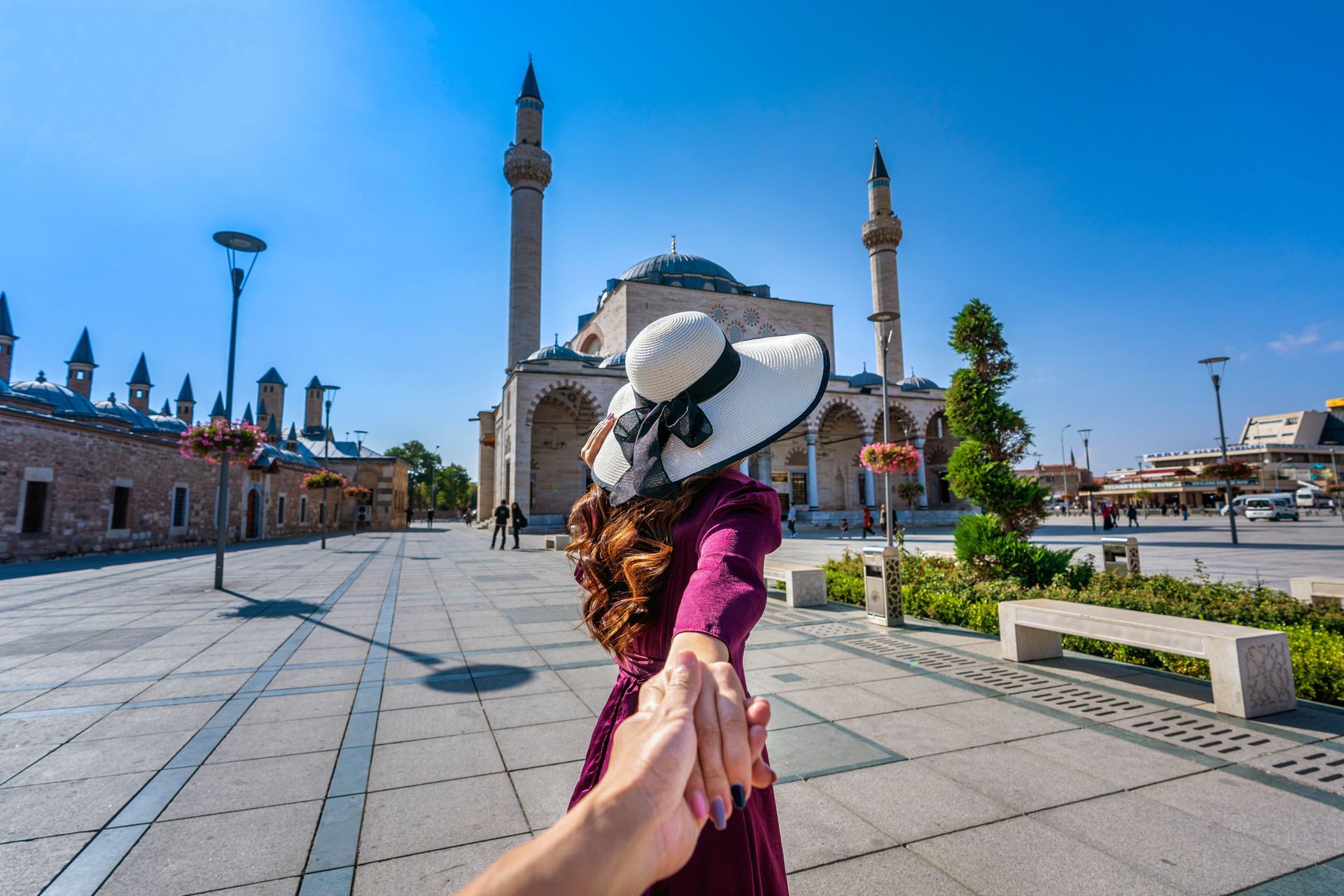 A woman in a hat is holding a man 's hand in front of a mosque.