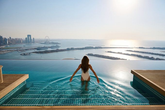 A woman is sitting in an infinity pool overlooking the ocean.