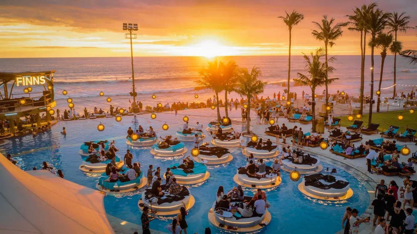 A large swimming pool filled with people at a beach at sunset.