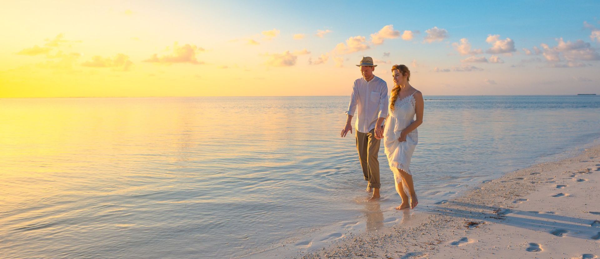 A man and a woman are walking on the beach at sunset.