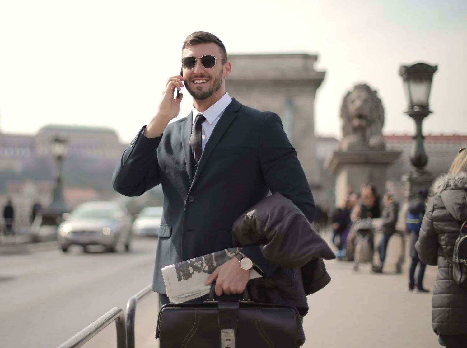 A man in a suit is talking on a cell phone while holding a briefcase.