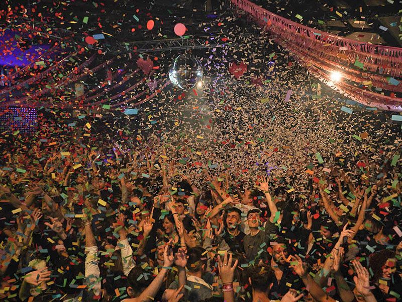 A crowd of people are gathered in a dark room with red lights.