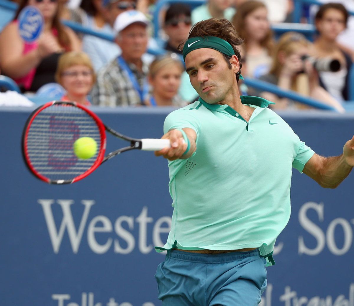 A man is playing tennis in front of a sign that says west