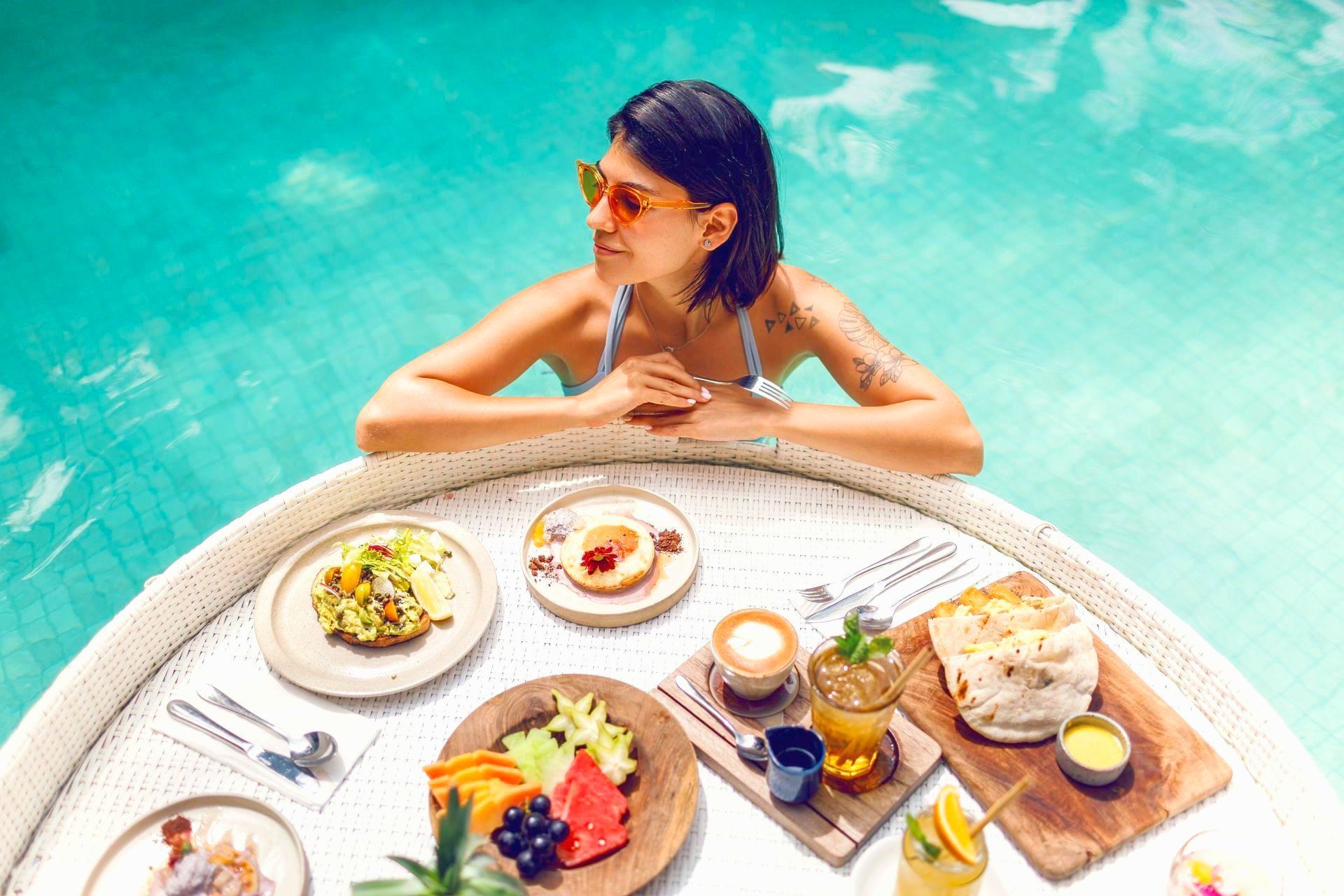 A woman is sitting at a table with food in a swimming pool.