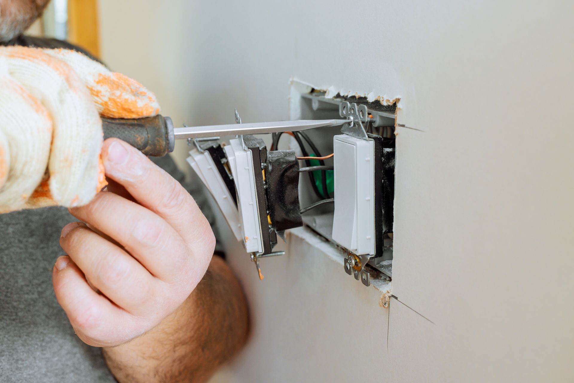 Hand installing a white electrical wall switch into a wall box
