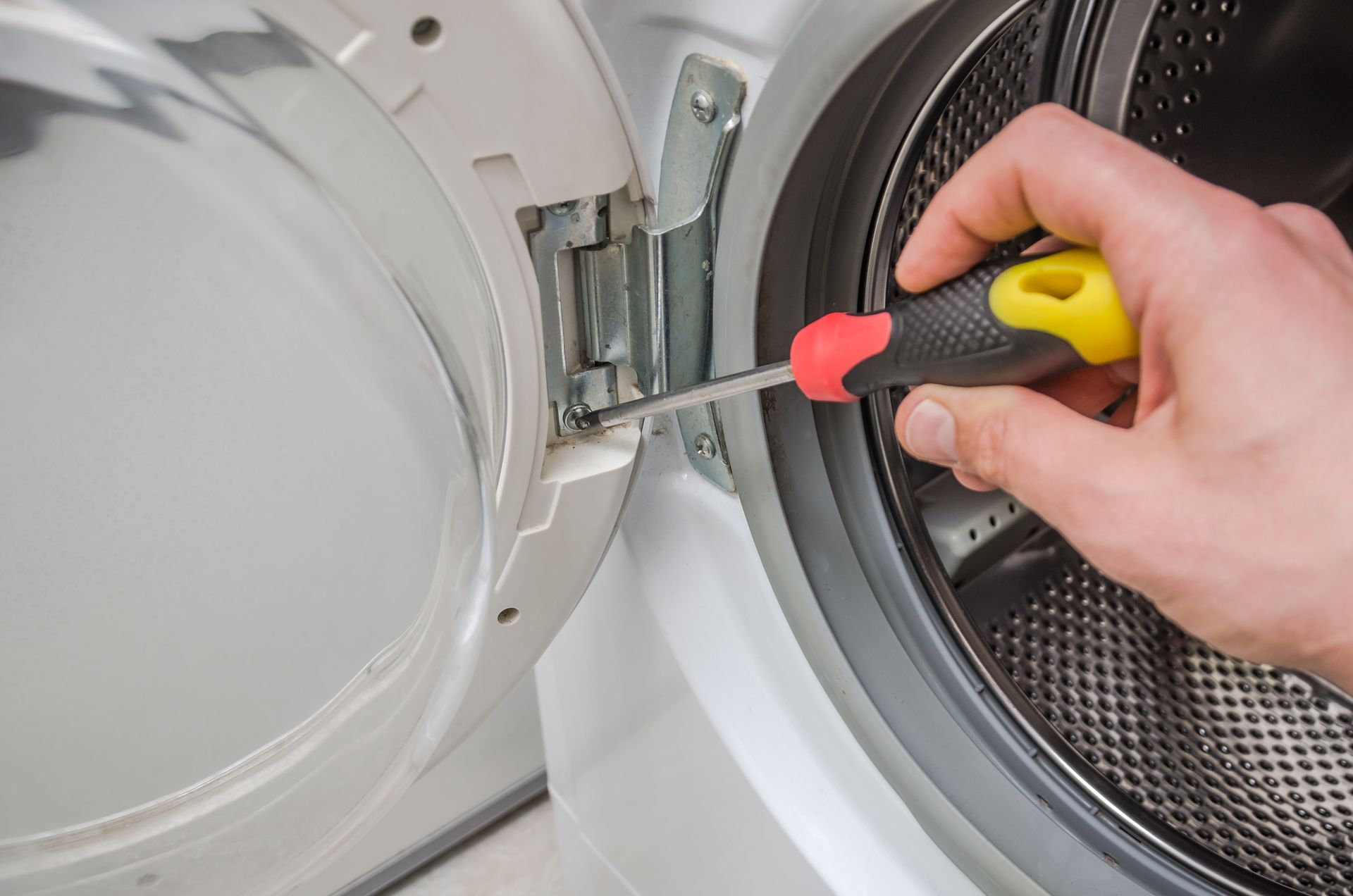 Hand using a screwdriver to repair a washing machine door latch