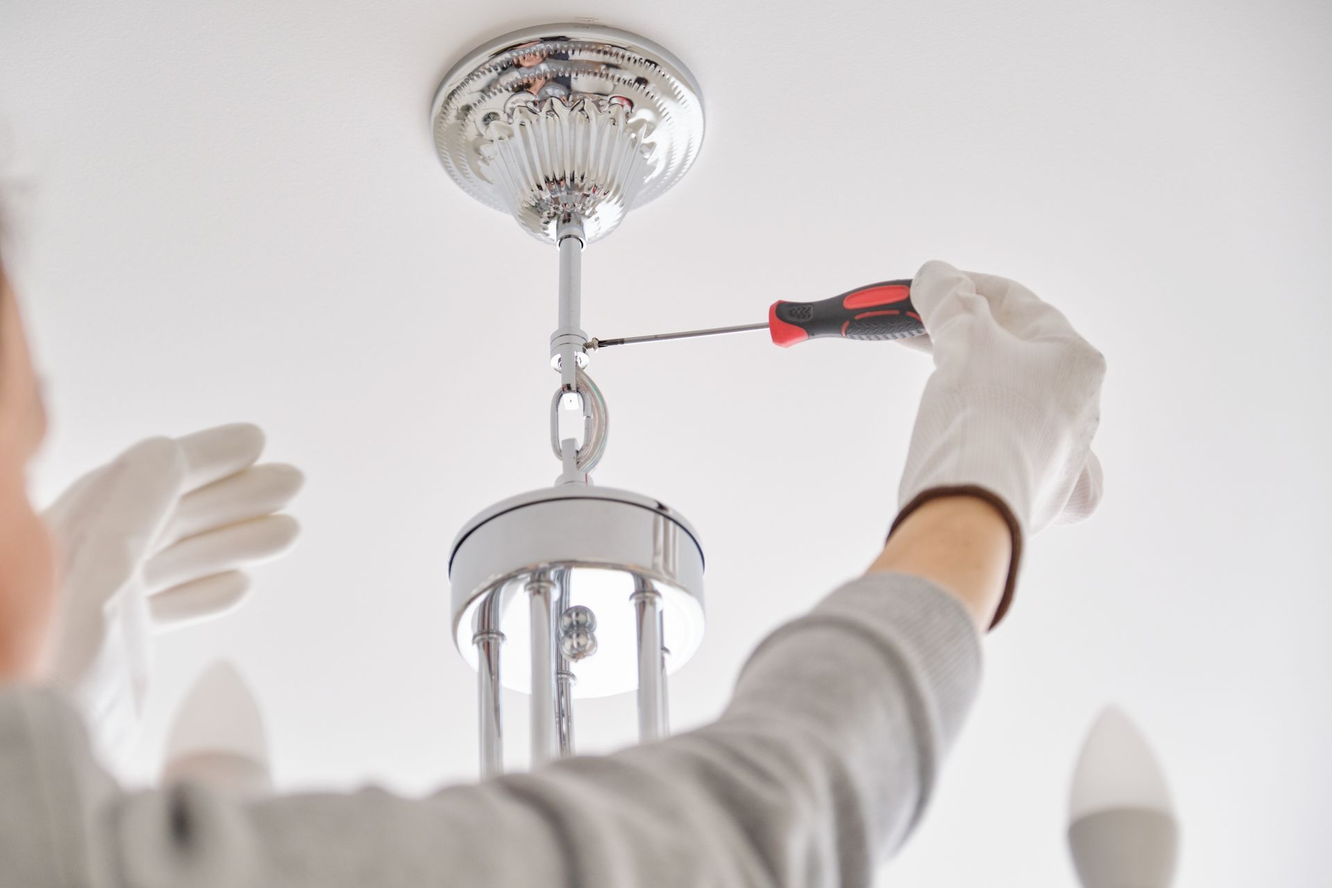Person using a screwdriver to tighten a hanging light fixture on a ceiling.