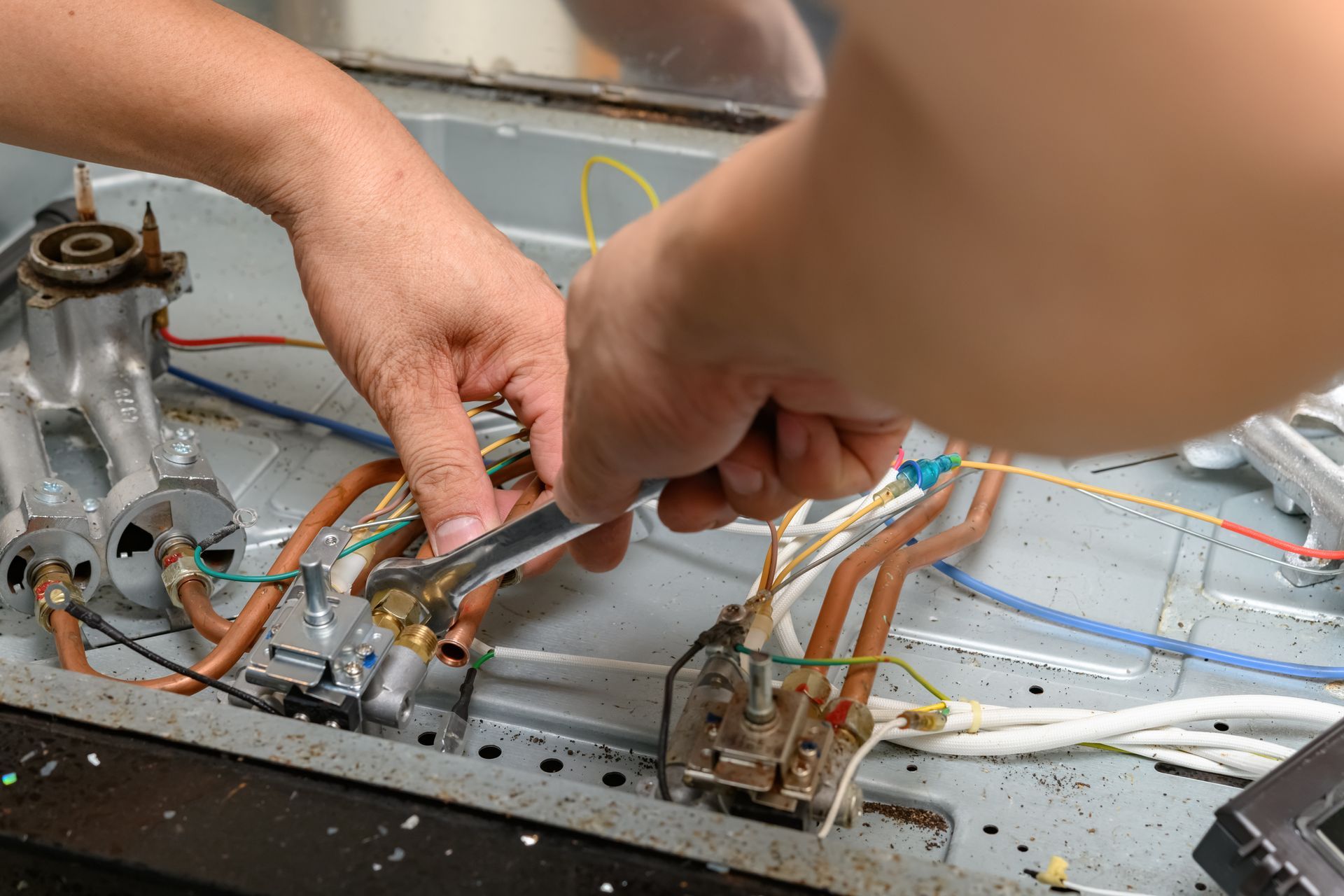 Hands repairing exposed electrical wiring inside a metal appliance
