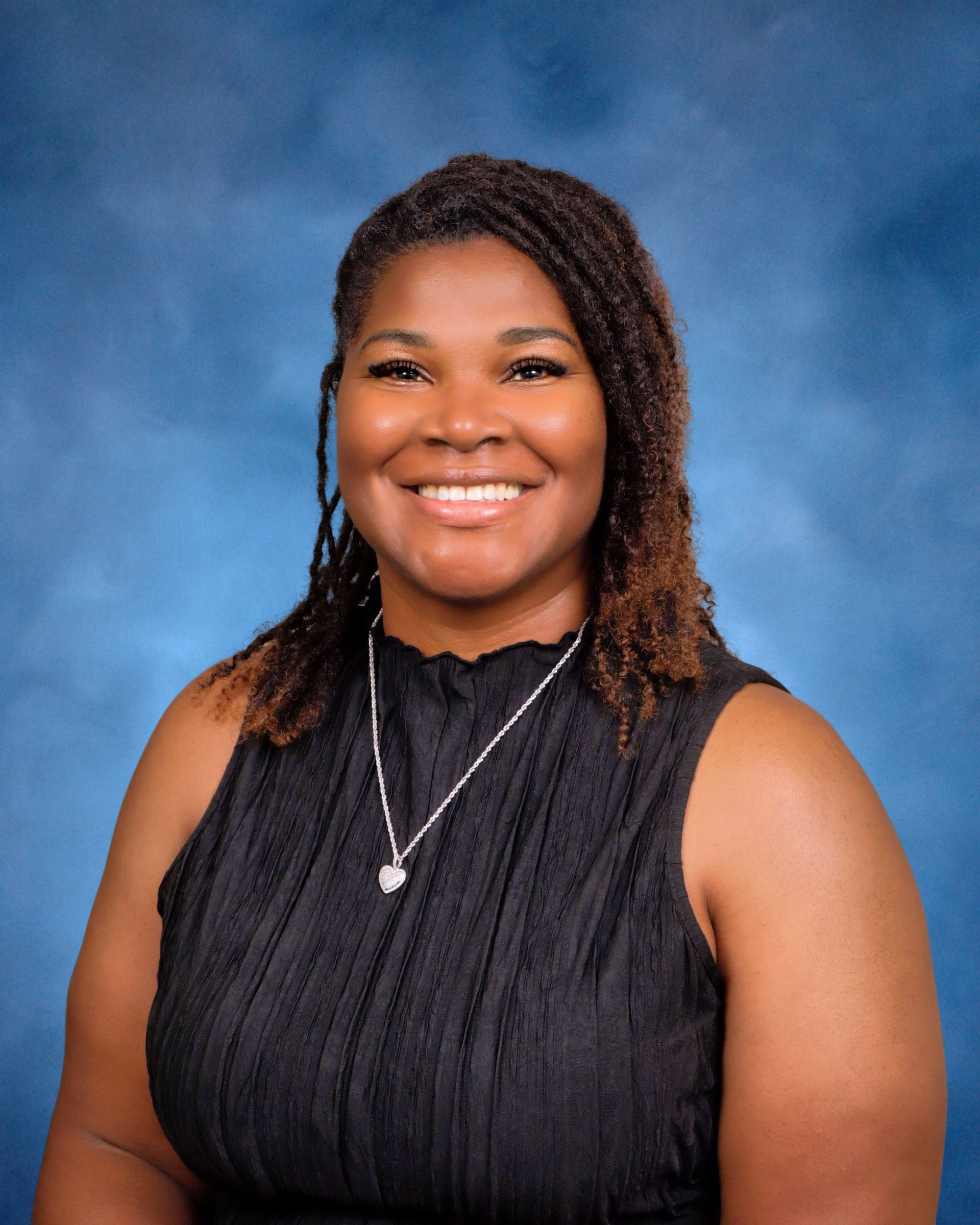 A woman wearing a black tank top and a necklace is smiling for the camera.