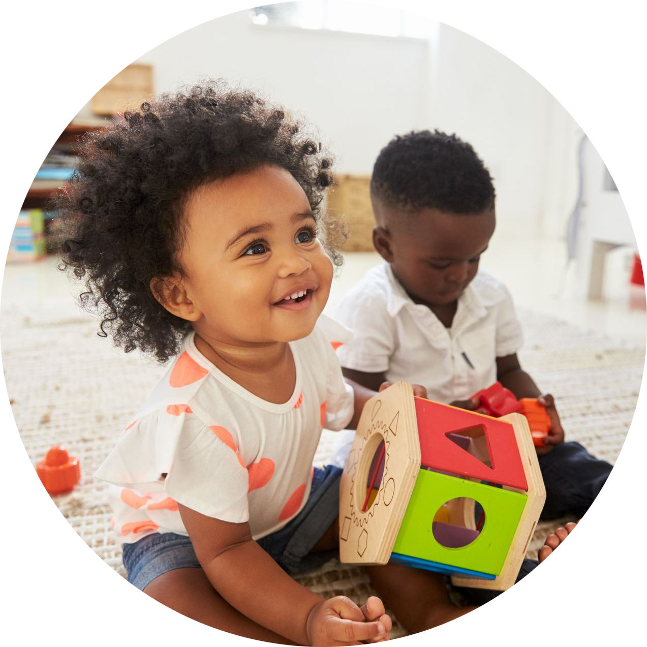 Two babies are sitting on the floor playing with toys.