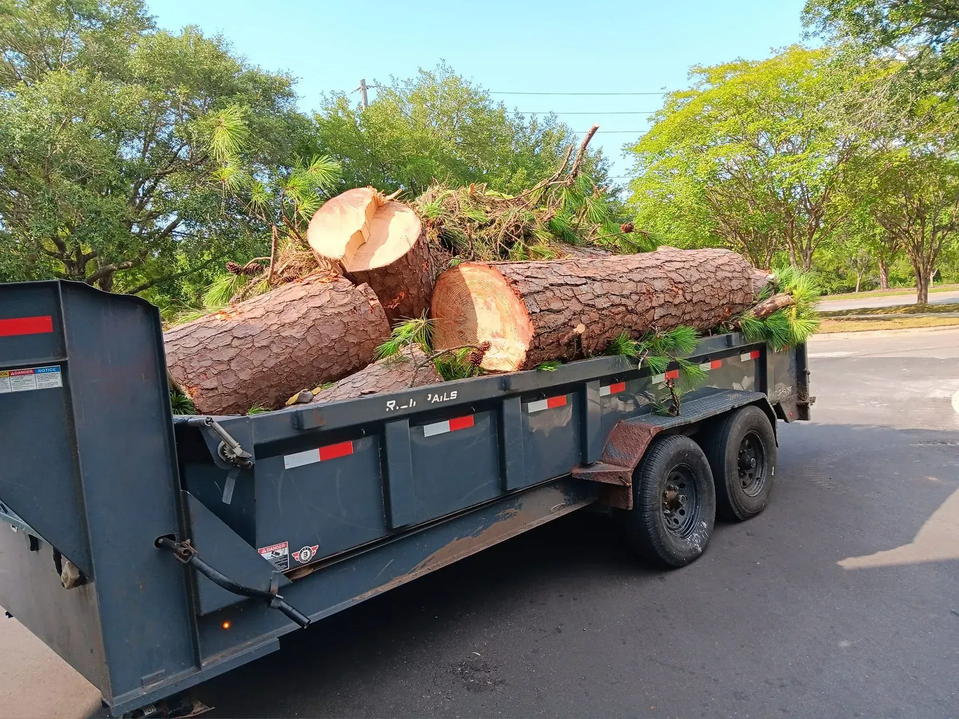 A dumpster filled with logs is parked on the side of the road.