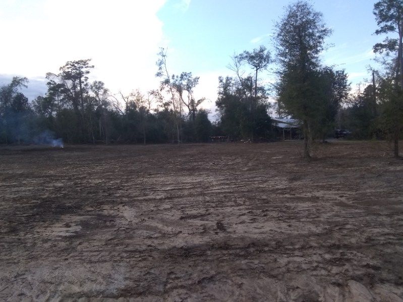 A dirt field with trees in the background and a house in the distance.